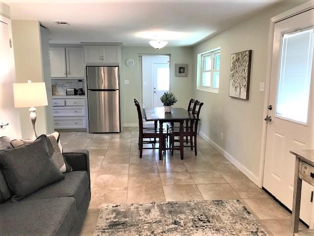 Open-plan dining area with a dark wood table, gray sofa, and kitchen with stainless steel appliances.