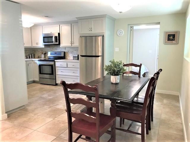Kitchen and dining area with stainless steel appliances and a dark table surrounded by wooden chairs.