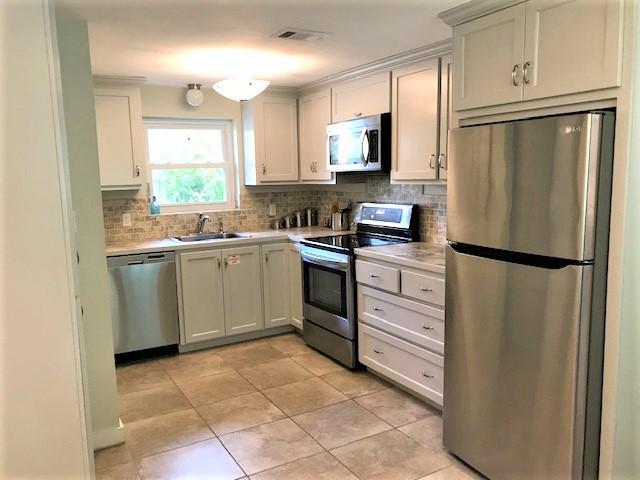 Kitchen with white cabinets, stainless steel appliances, and a tiled backsplash and floor.