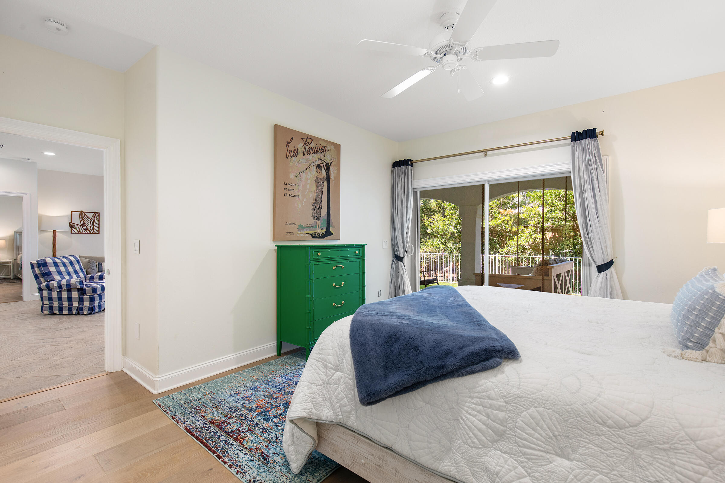 Bedroom with a white quilted bed, green dresser, and sliding doors to a leafy covered balcony.