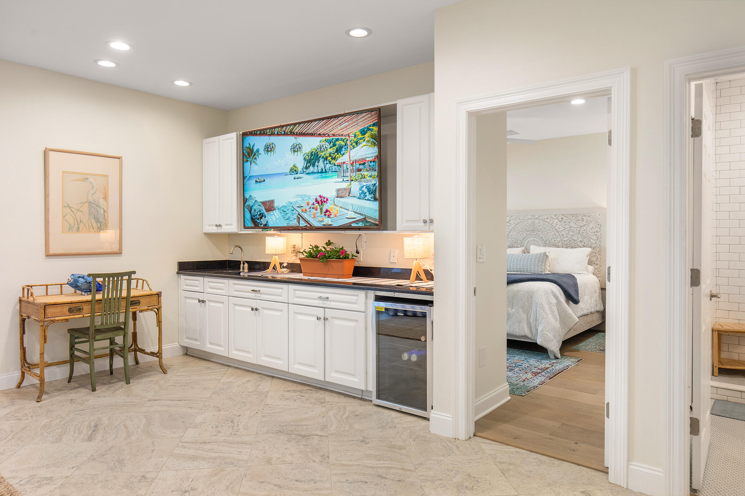Kitchenette with white cabinets and a beverage fridge, beside open doorways to a bedroom and bathroom.