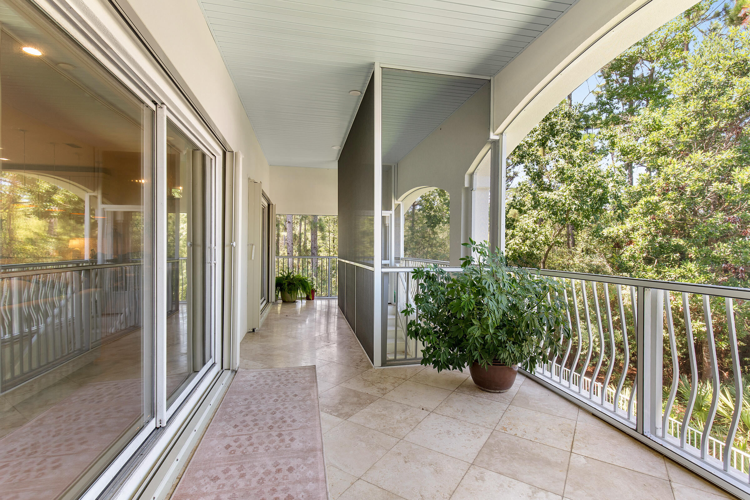 Covered balcony with tiled floor and white railing overlooking leafy trees.