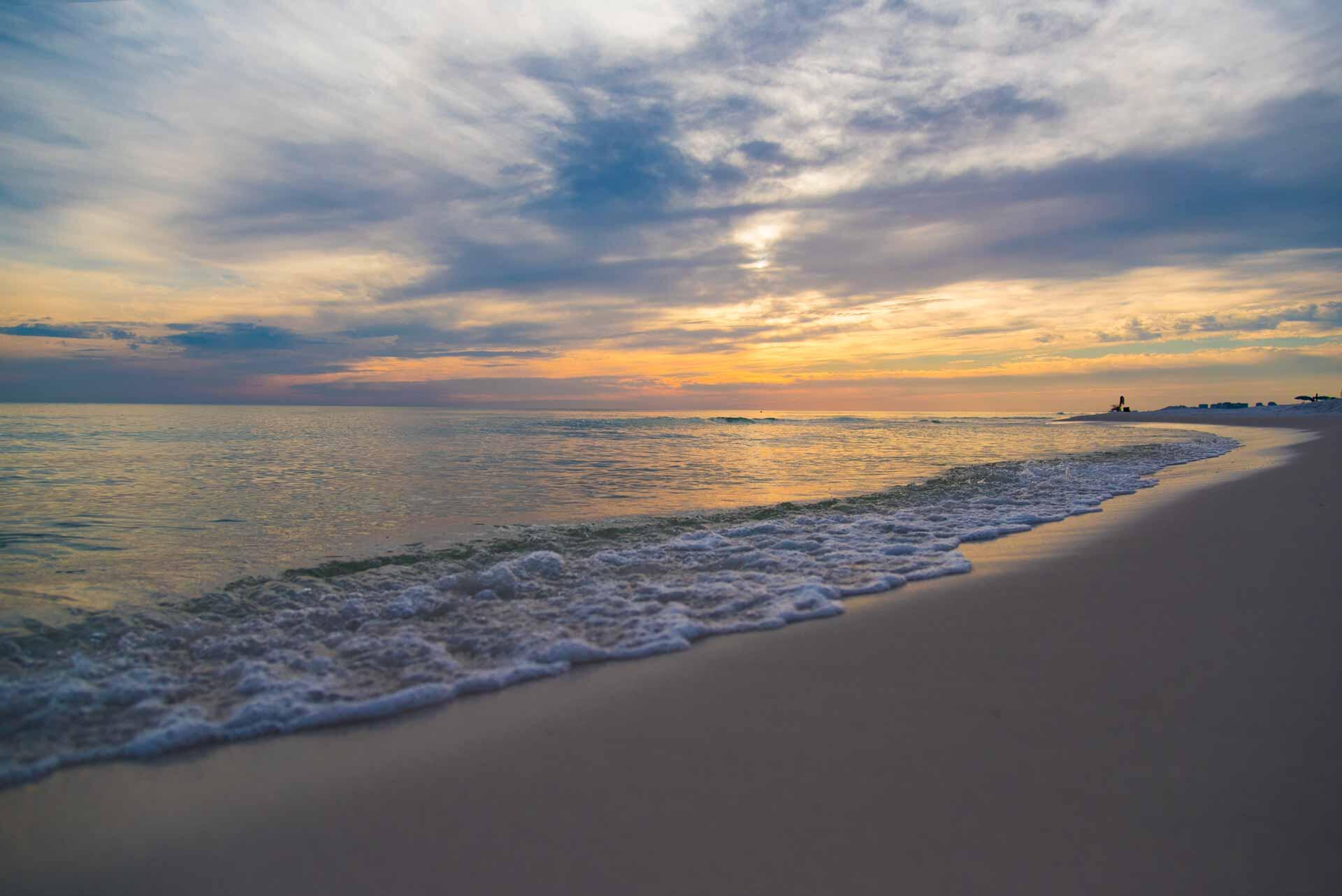 Waves wash onto a sandy beach beneath a colorful dusk sky.