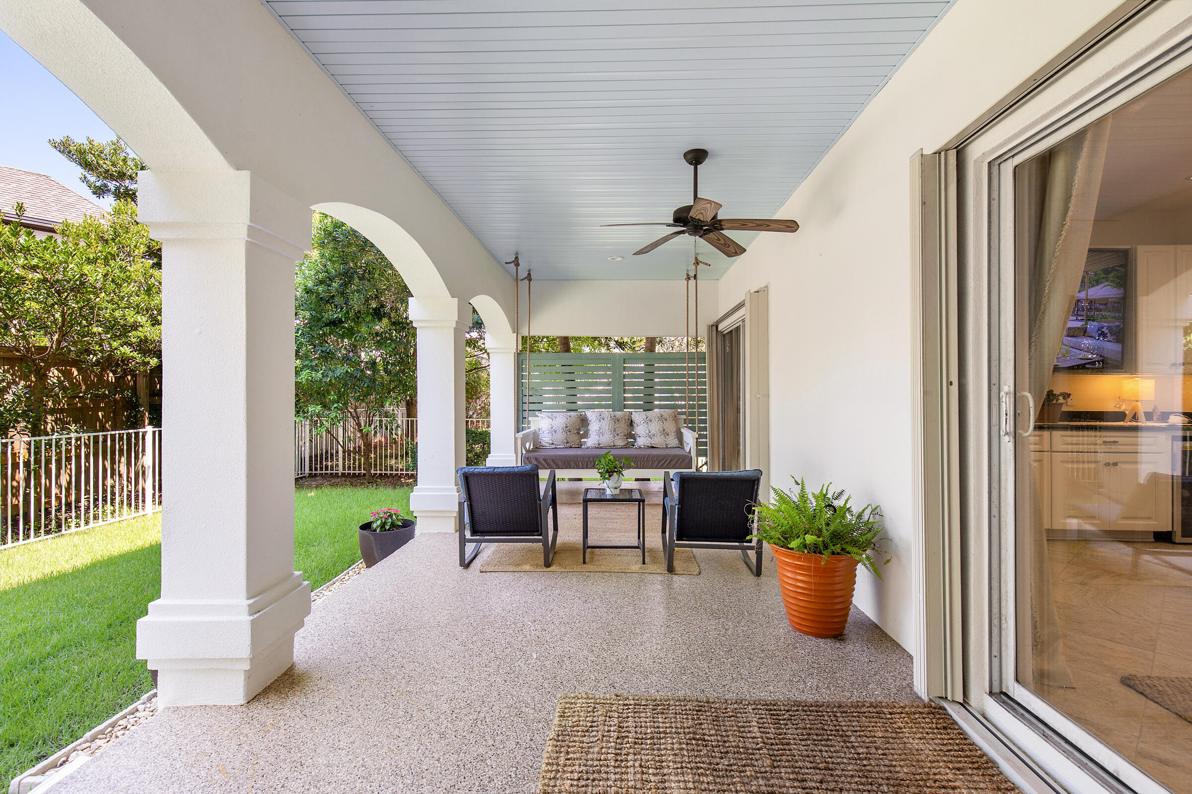 Covered patio with white arches, ceiling fan, and outdoor seating beside a green yard.