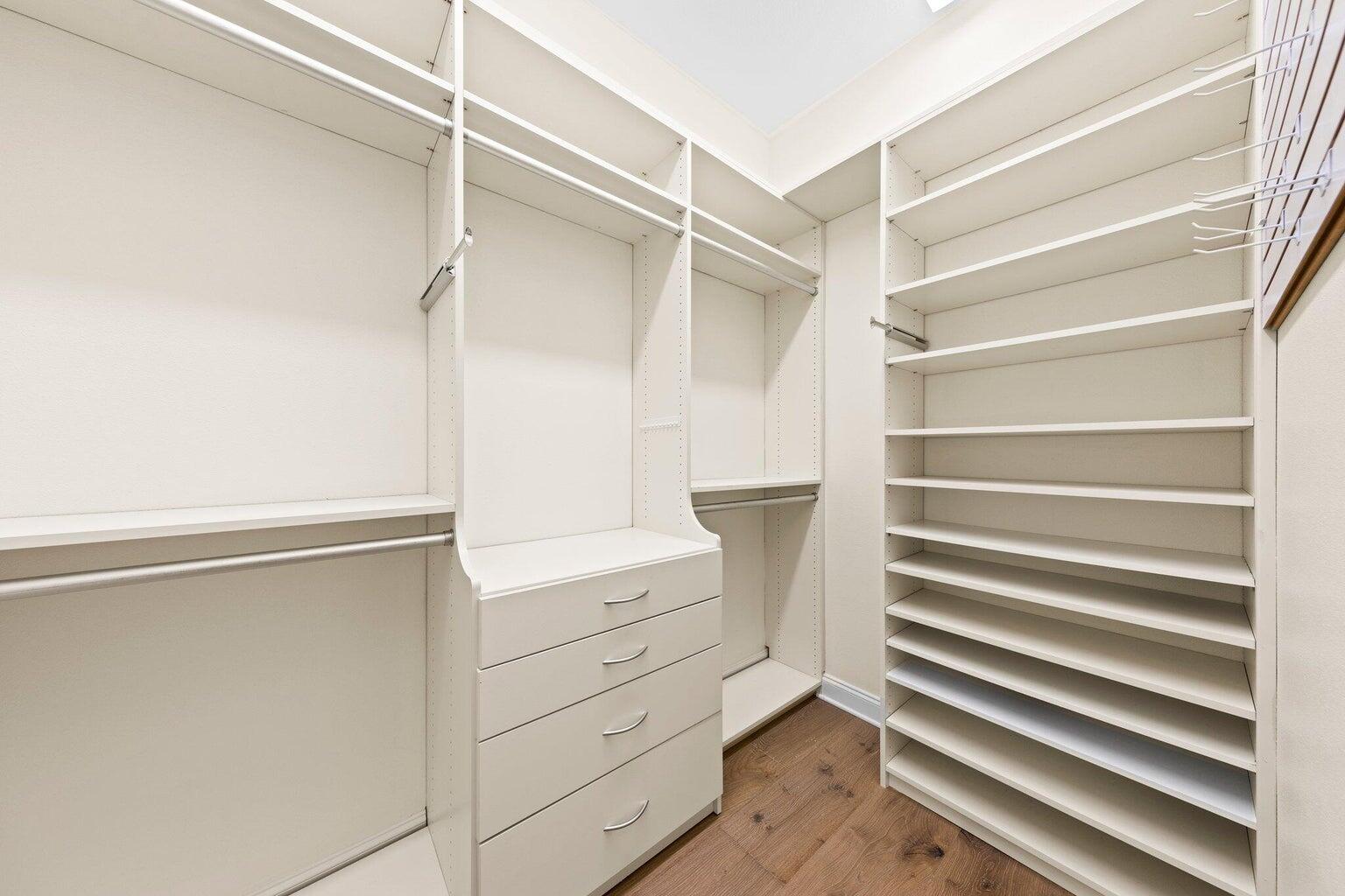 Walk-in closet with white built-in drawers, hanging rods, and angled shoe shelves.