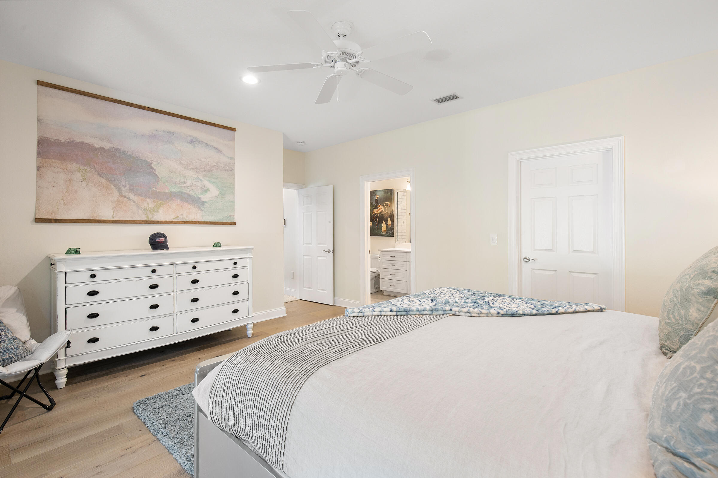 Furnished bedroom with a large white bed, dresser, and open doorway to an adjoining bathroom.