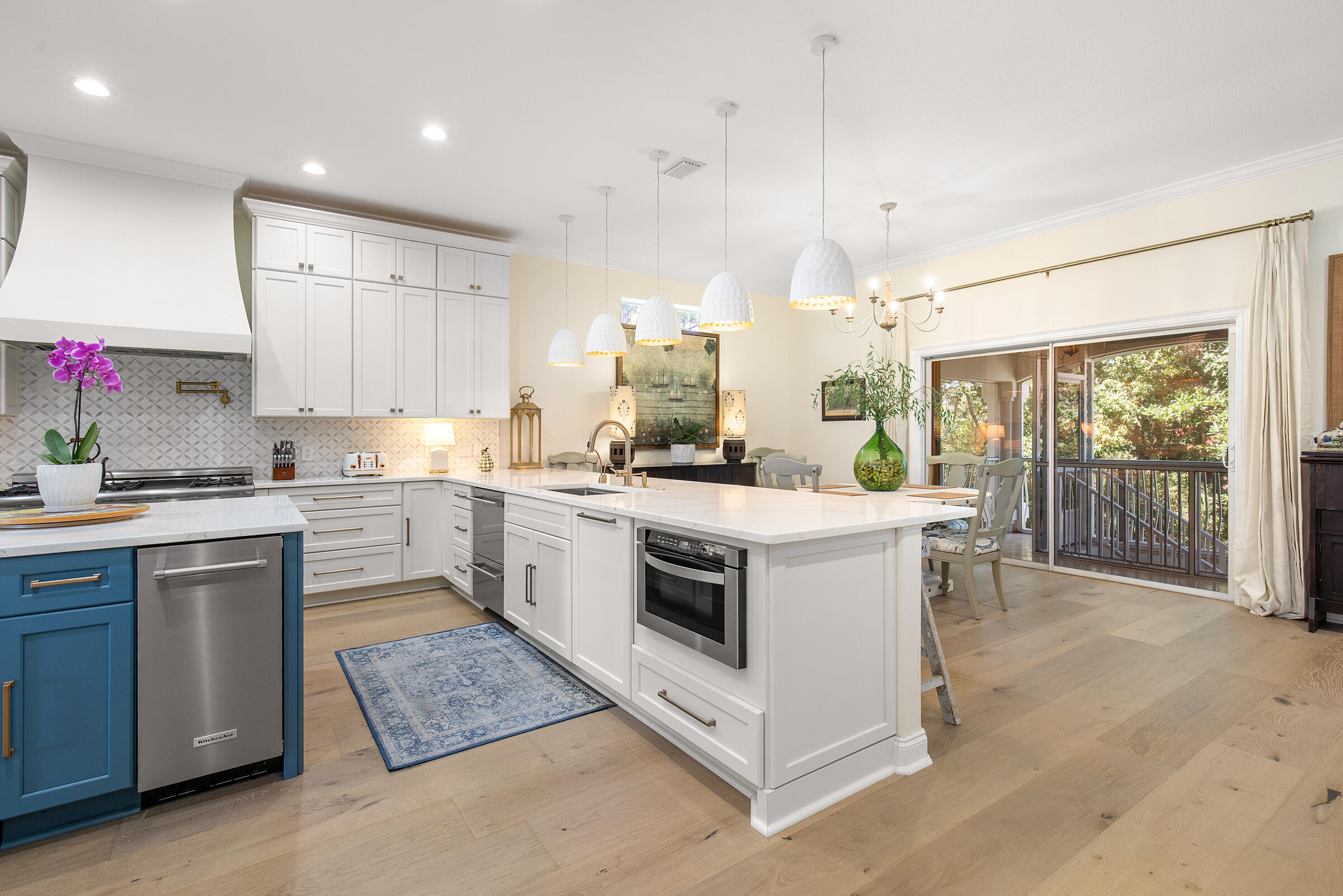 Bright kitchen with a large white island, blue lower cabinets, and sliding doors opening to a screened porch.
