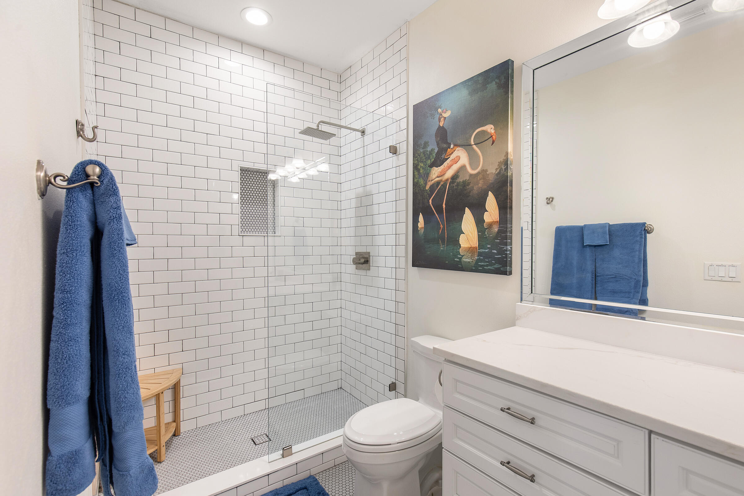 Bathroom with a white subway-tile shower, glass enclosure, long vanity, and blue towels.