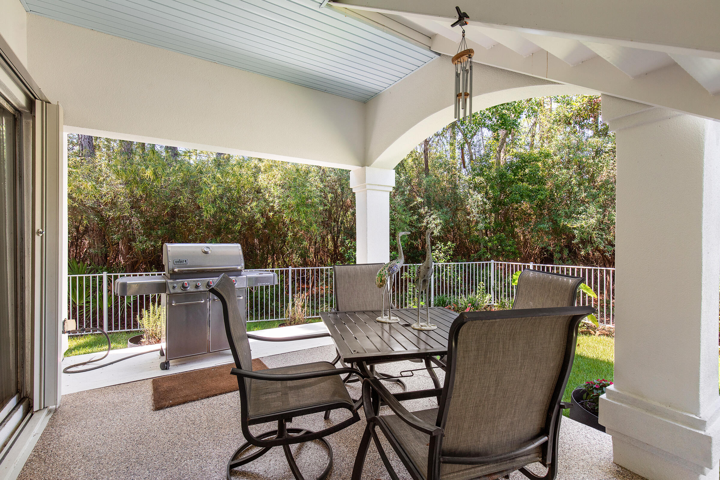 Covered patio with dining furniture and a gas grill overlooking a fenced, wooded yard.