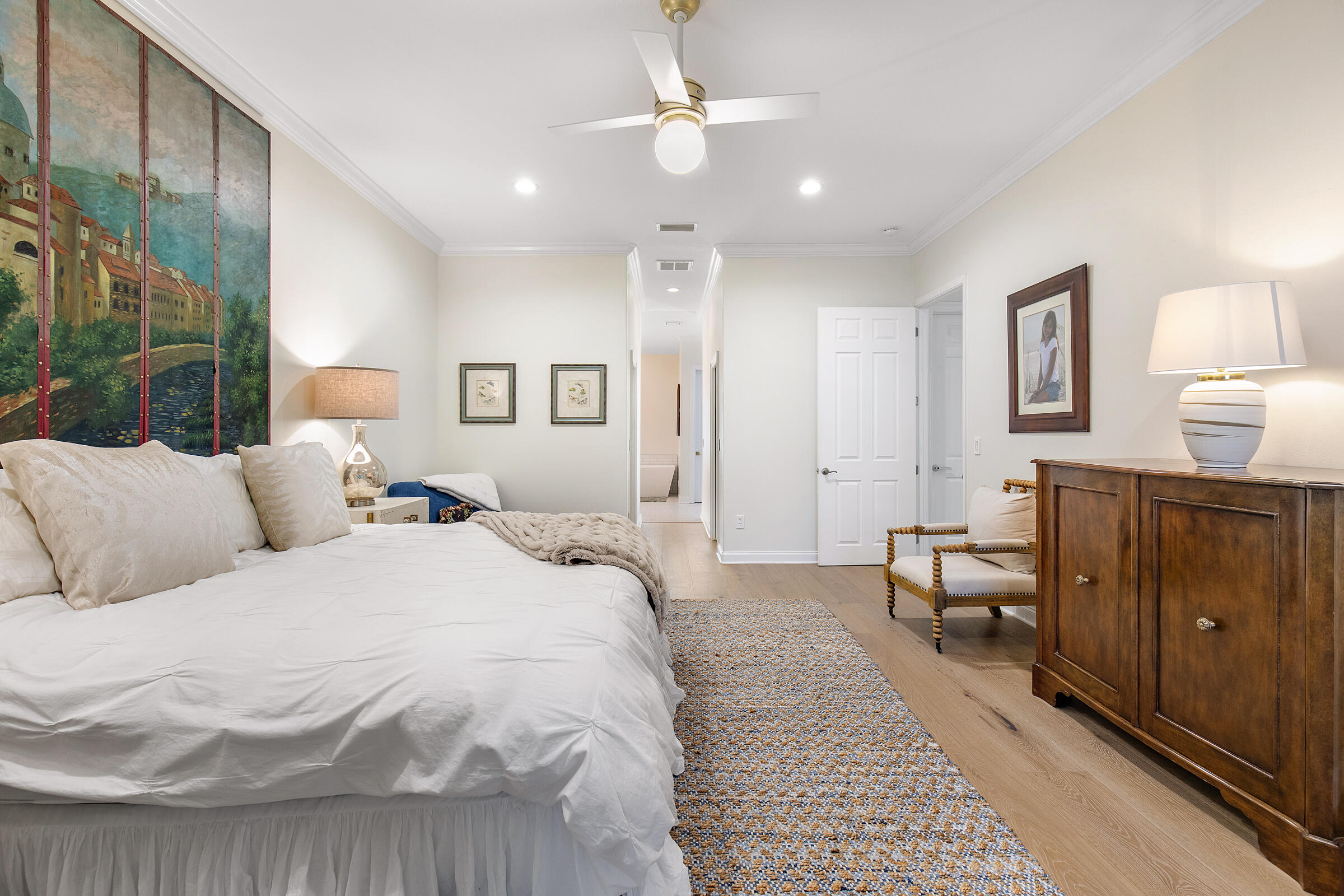 Furnished bedroom with a large white bed, colorful rug, and floor-to-ceiling painted mural.