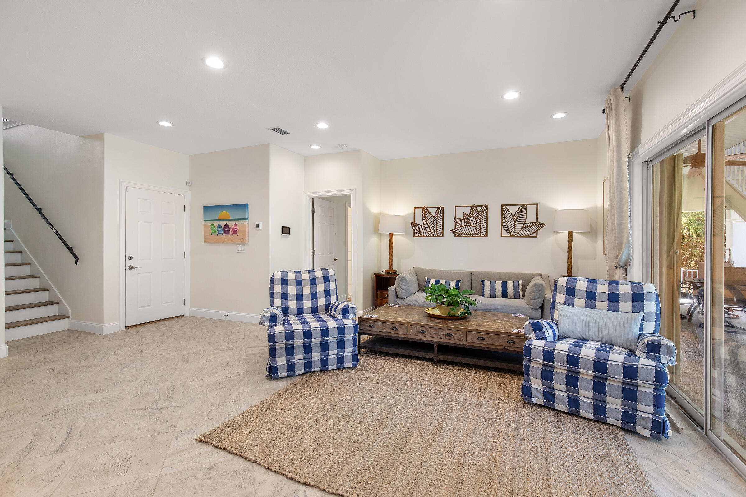 Furnished living room with blue checkered armchairs, a gray sofa, and sliding glass doors.
