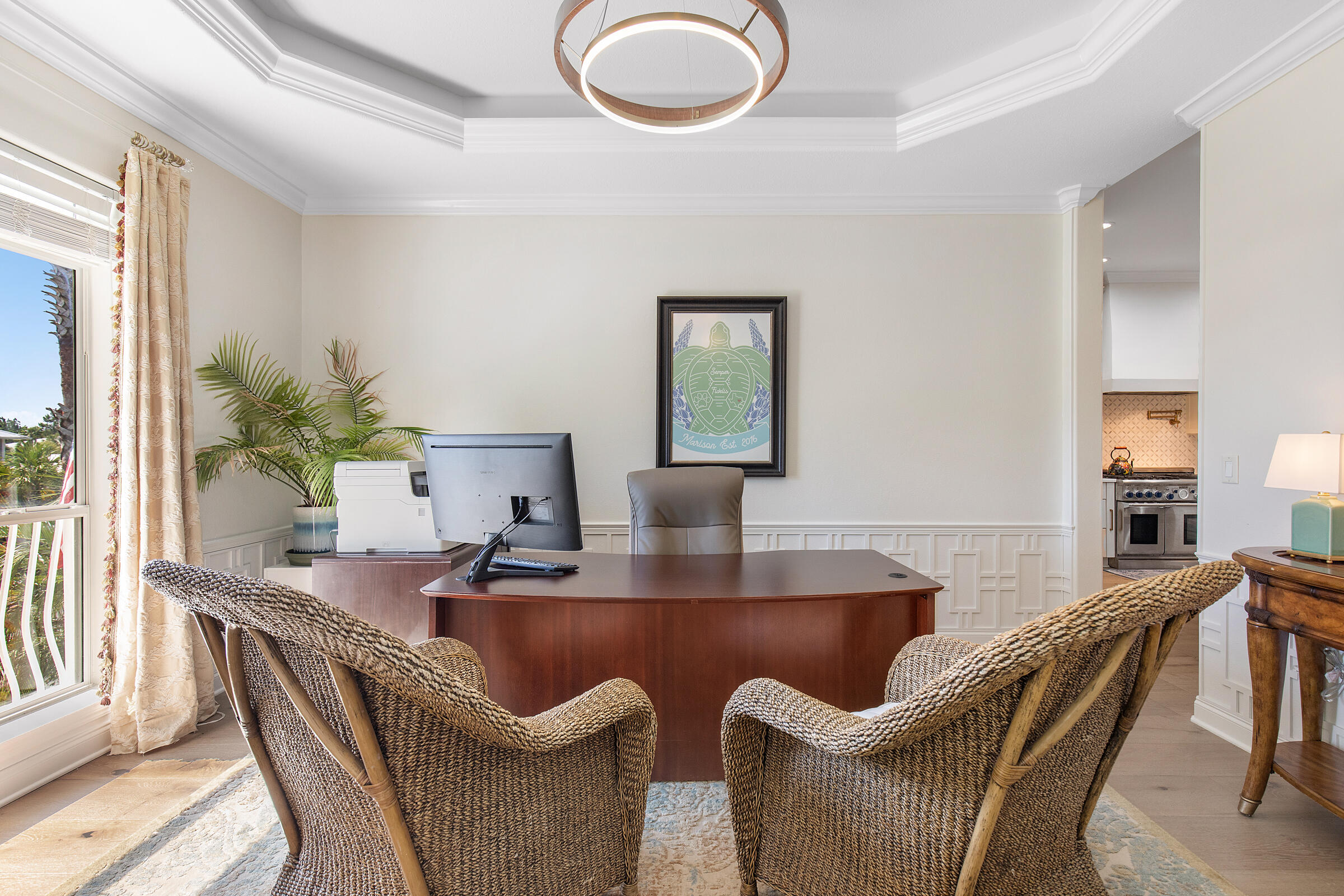Home office with a curved wooden desk, woven chairs, and bright window.