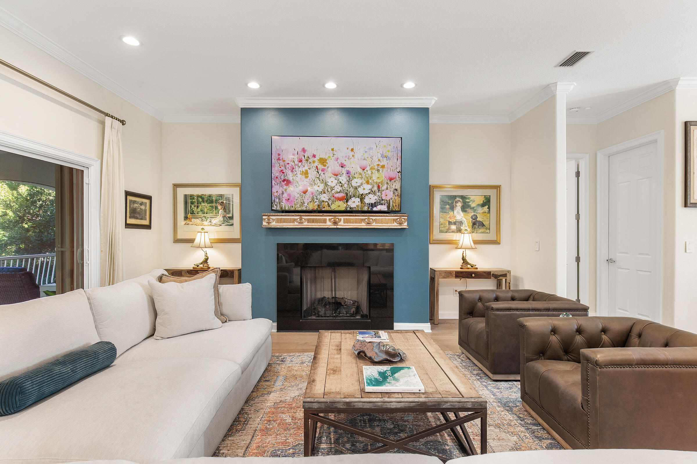 Living room with a blue fireplace wall, cream sofa, brown leather chairs, and sliding glass door to a balcony.