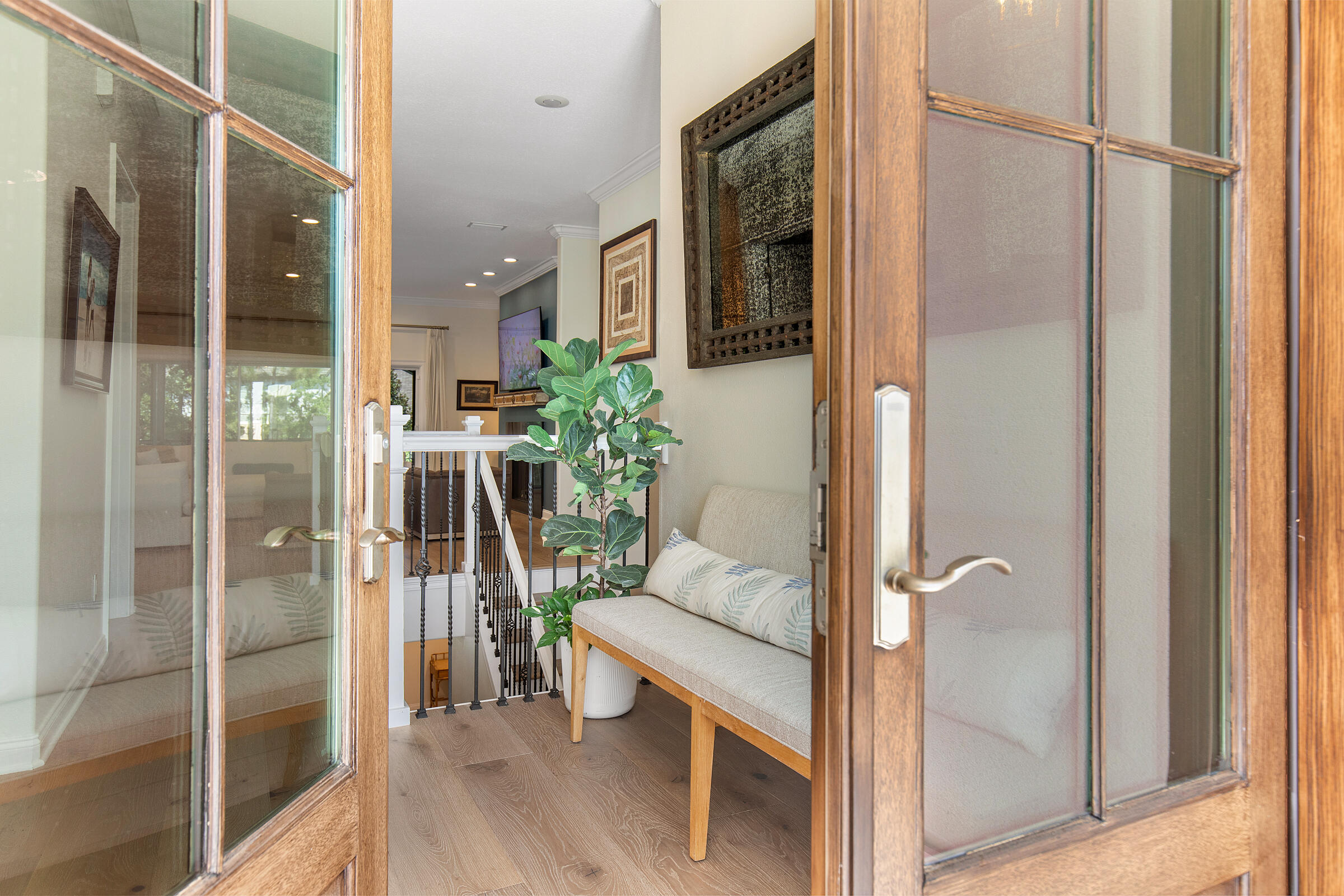 Entry foyer with open wood-framed glass doors, a cushioned bench, and a potted plant.