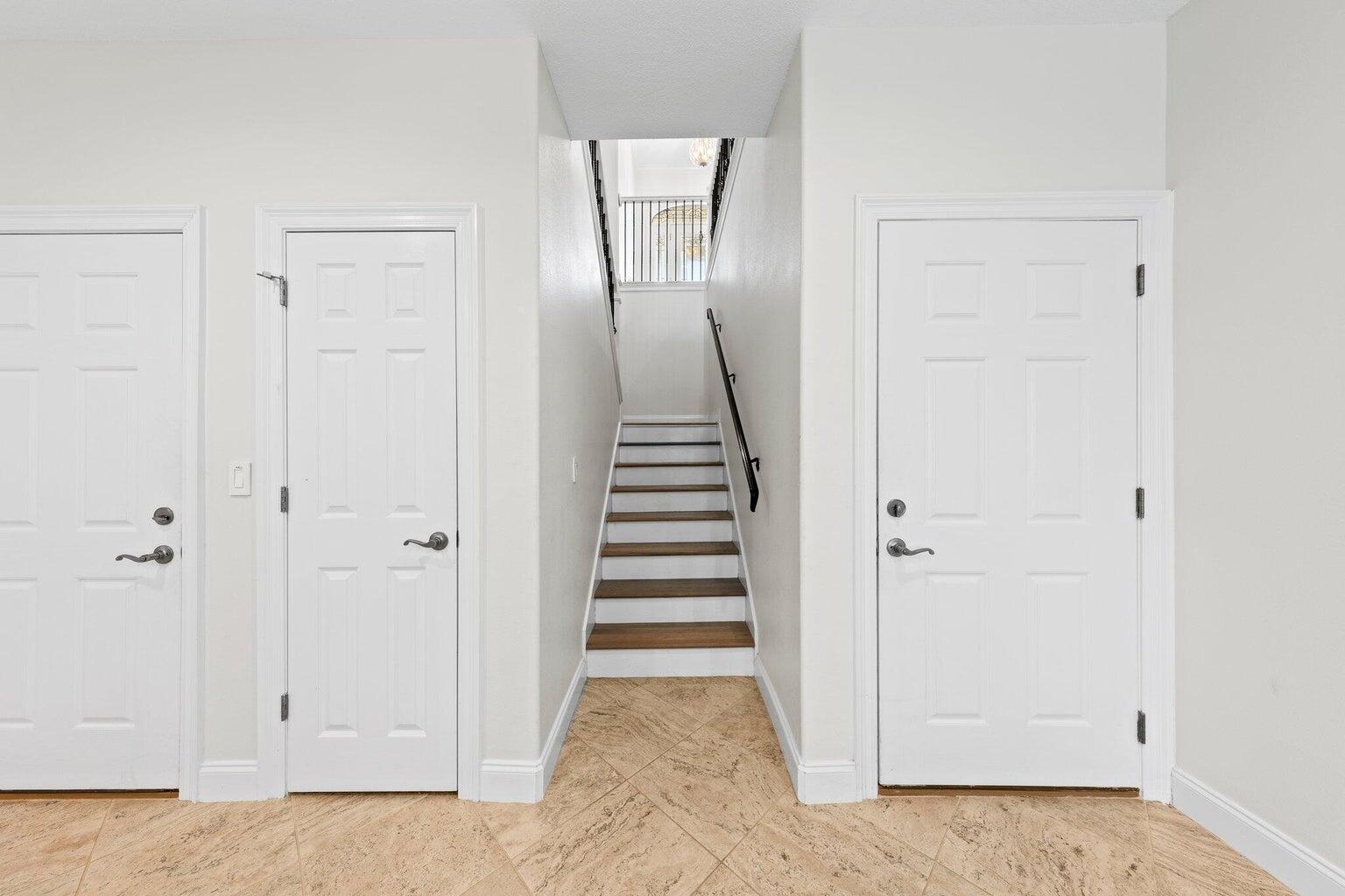 Hallway with tiled floors, three white doors, and a staircase with dark wood treads.