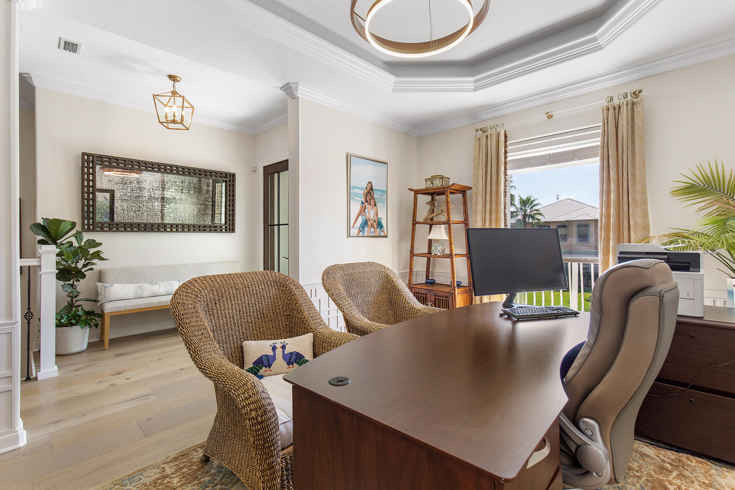Furnished home office with a dark wood desk, wicker chairs, and a bright curtained window.