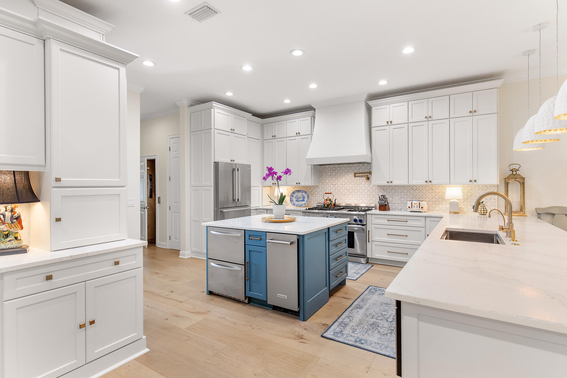 Bright kitchen with white cabinetry, a blue appliance-equipped island, and marble-look counters.
