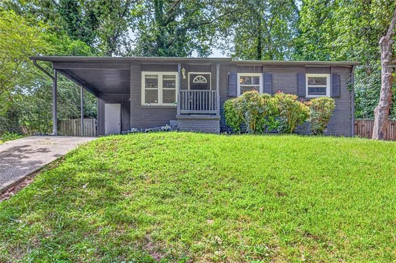 Single-story dark-sided house with a covered carport, small front porch, and broad green lawn.