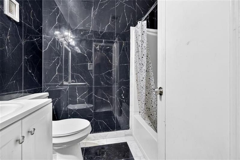 Bathroom with black marble-look tile, glass shower enclosure, and white vanity.