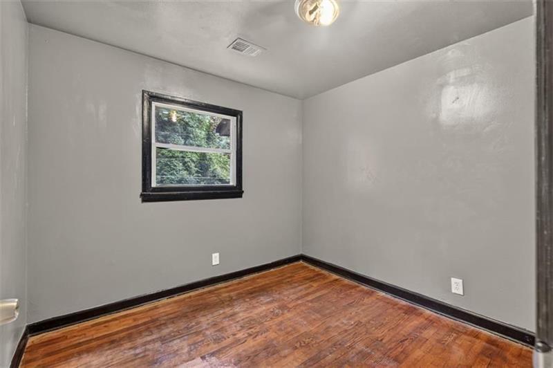 Empty room with polished hardwood floors, gray walls, and a window.