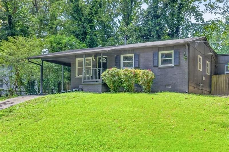 Single-story dark-sided house with a covered carport, front porch, and broad green lawn.