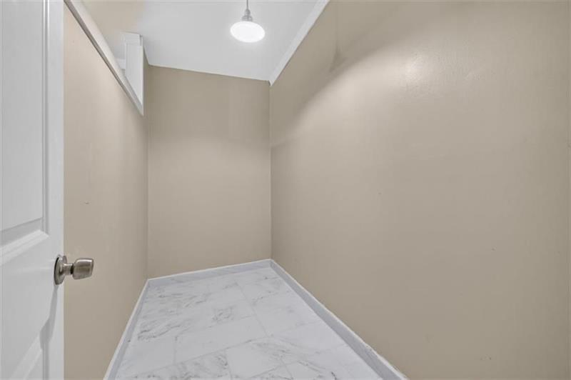 Empty closet with beige walls, marble-patterned tile floor, and a ceiling light.