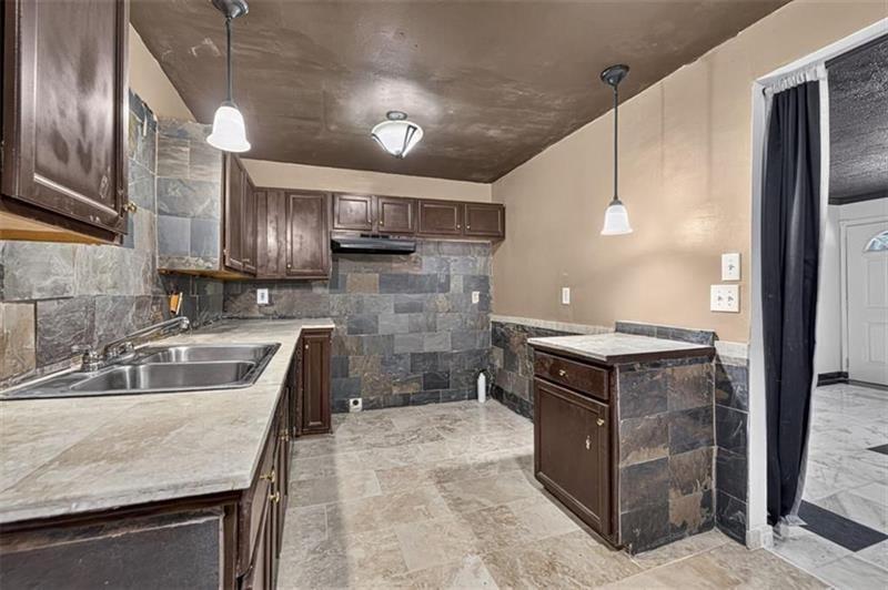 Kitchen with slate tile walls, dark wood cabinets, stone counters, and a peninsula.