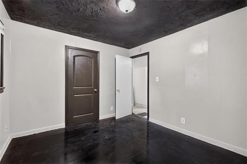 Empty room with gray walls, a dark textured ceiling, and dark flooring.