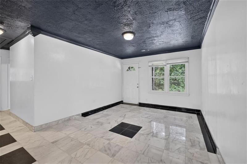 Empty tiled room with a dark textured ceiling, exterior door, and window.