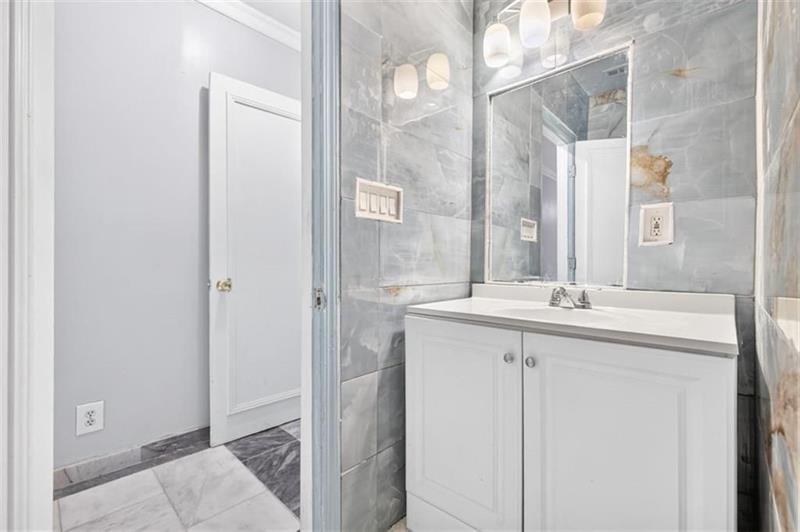 Bathroom with gray marble-look tile and white vanity, seen through an open doorway.