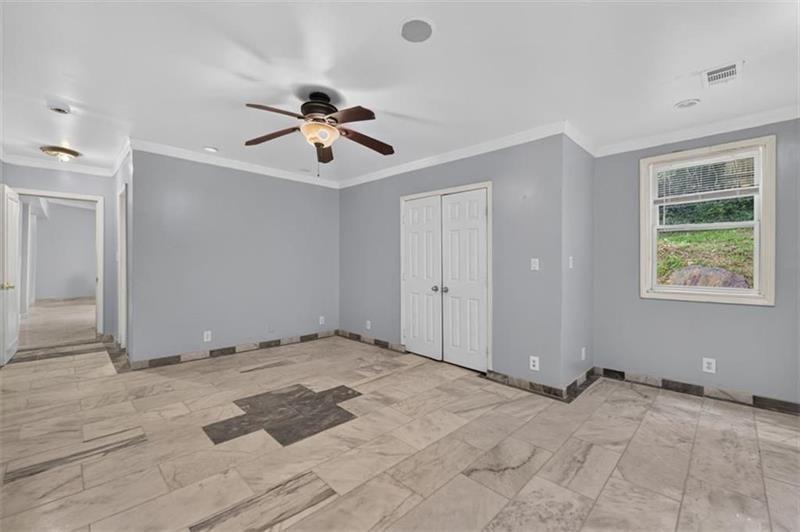 Empty room with gray walls, patterned tile flooring, a ceiling fan, and double closet doors.