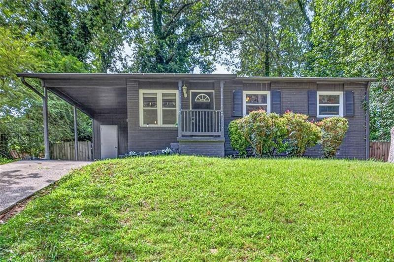 Single-story dark-sided home with a covered carport, small porch, and broad green lawn.
