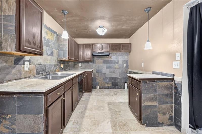 Vacant kitchen with dark wood cabinets, gray stone tile, a stainless steel sink, and a central peninsula.