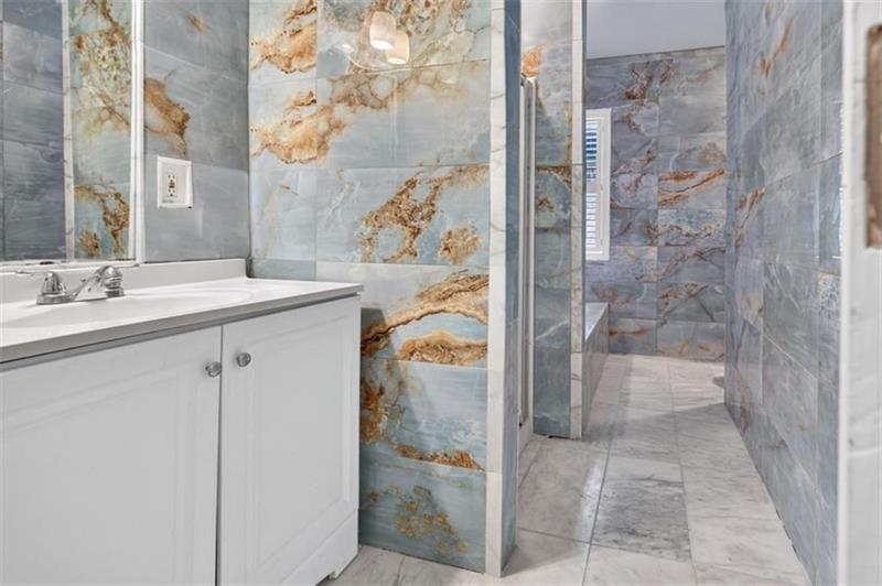 Bathroom with a white vanity and walk-in shower, finished in blue-gray tile with gold veining.