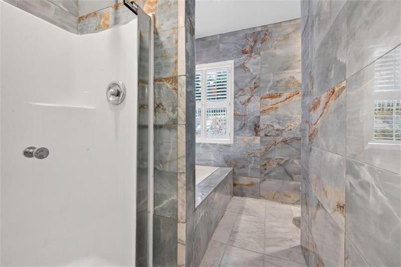 Marble-tiled bathroom with a glass shower enclosure, built-in bench, and shuttered window.