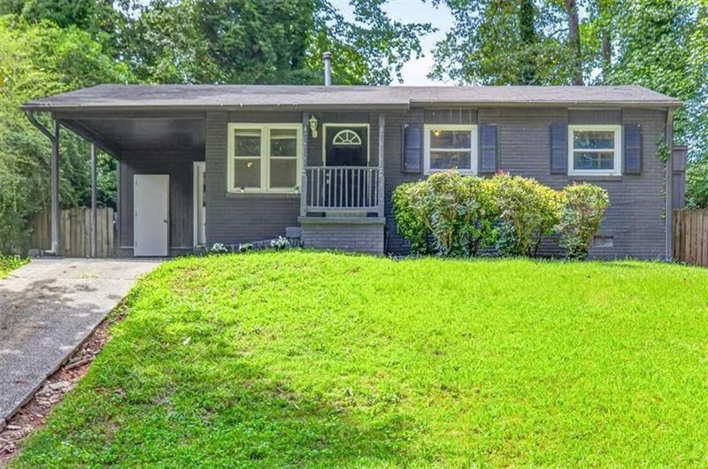 Single-story dark-sided house with a covered carport, small porch, and broad green lawn.