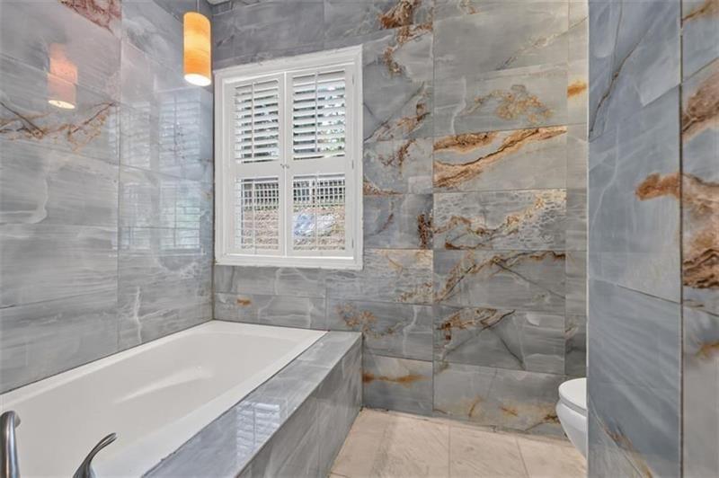Bathroom with a built-in soaking tub, gray veined tile, and a shuttered window.