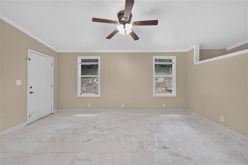 Empty room with marble-look tile flooring, two windows, and a ceiling fan.
