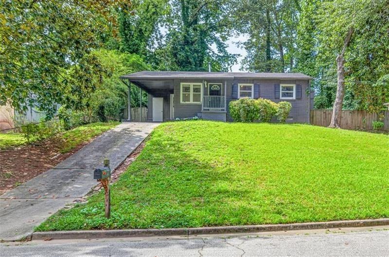 Gray single-story house with a covered entry, broad green lawn, and driveway.