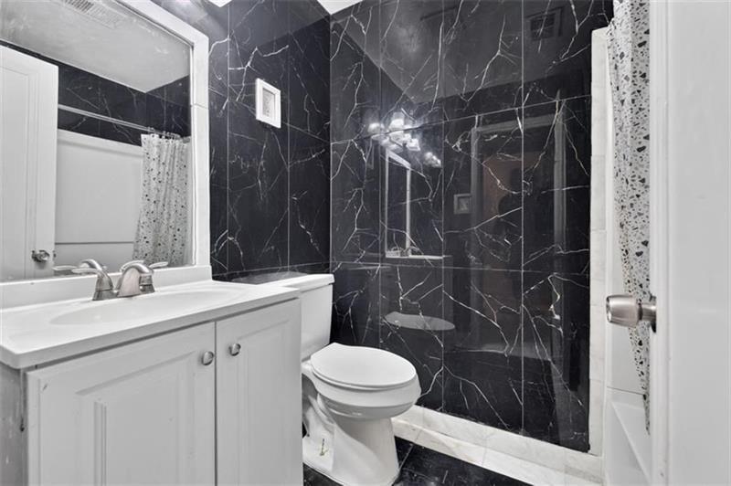 Bathroom with a white vanity and toilet beside a black marble-look tiled shower.