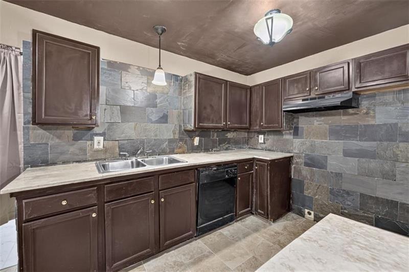 Kitchen with dark wood cabinets, gray stone tile backsplash, pale countertops, and a double-basin sink.