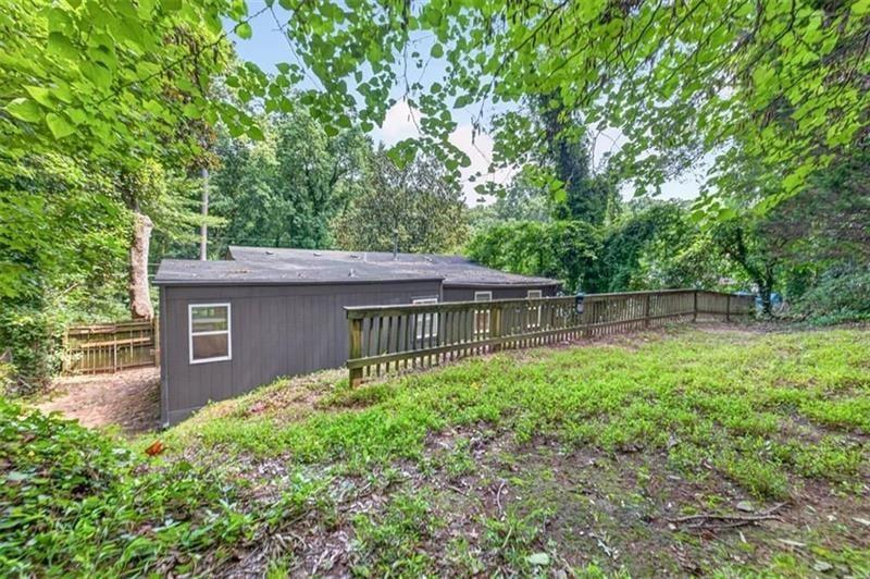 Dark gray house with a long wooden deck and railing in a wooded yard.
