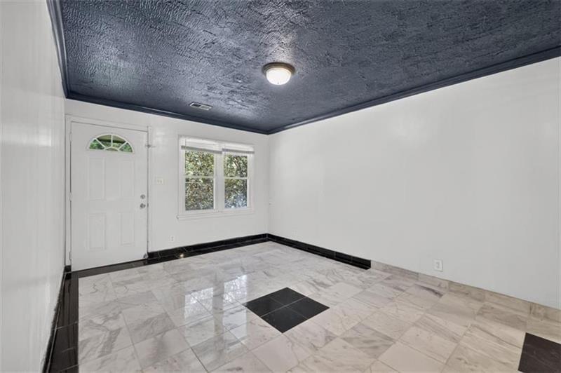 Empty entry room with marble-pattern tile floors, black trim, and a dark textured ceiling.