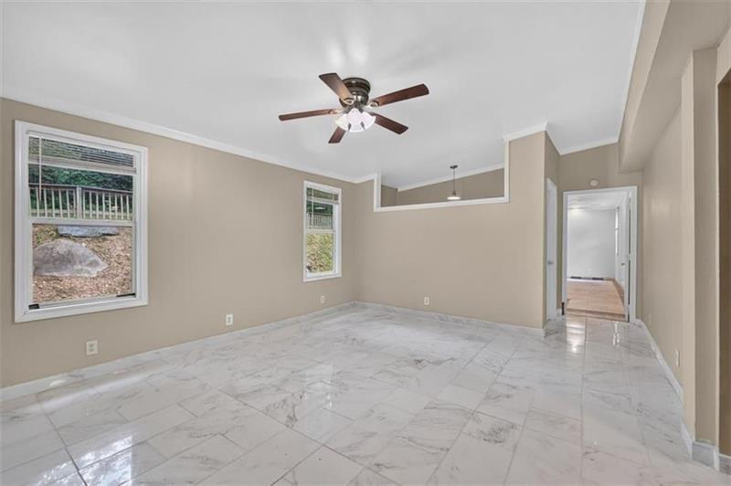 Empty living room with marble-look tile floors, a ceiling fan, and two windows.