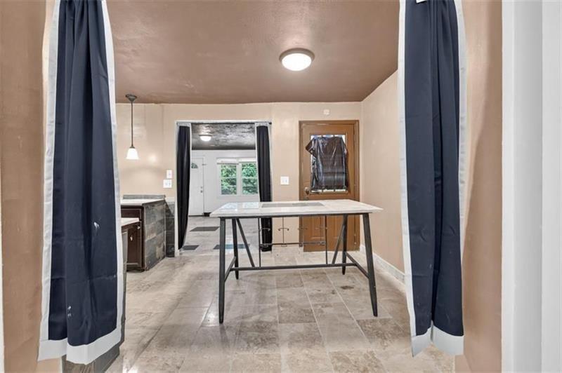 Kitchen with gray tile floors, dark doorway curtains, and a freestanding worktable.