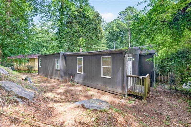 Single-story gray home with a small wooden porch on a wooded lot.