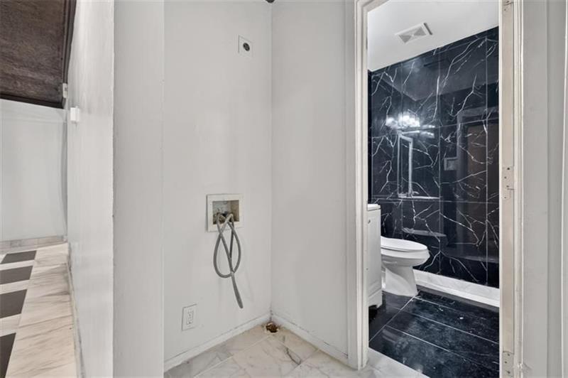 Bathroom with black marble tile and toilet, adjoining a light-colored area with exposed plumbing hookups.