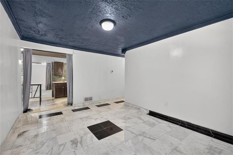Empty tiled room with a dark ceiling and curtained doorway to the kitchen.