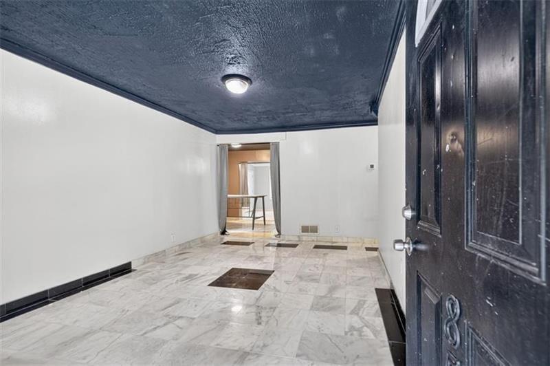 Empty tiled interior with a dark ceiling, black paneled door marked 8, and a doorway to another room.