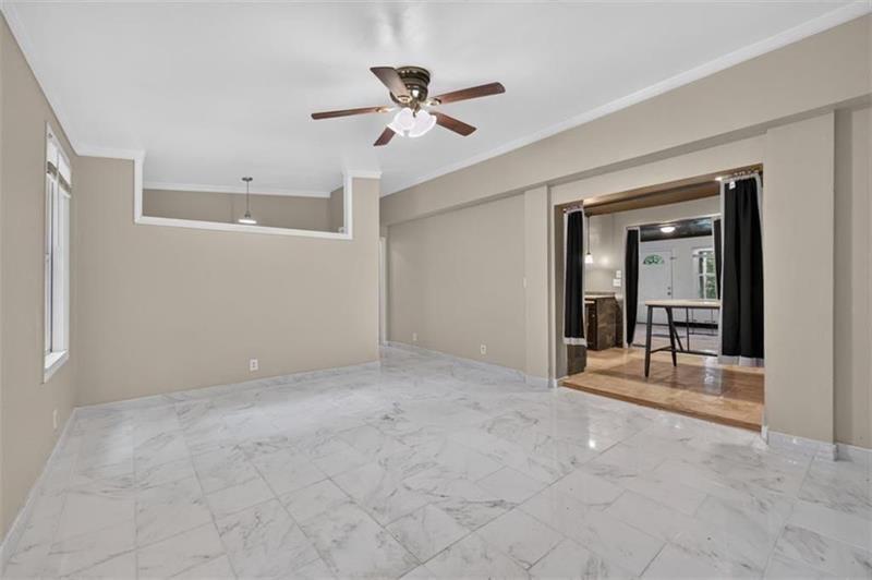Vacant living room with marble-look tile floors, a ceiling fan, and an opening to an adjoining room.